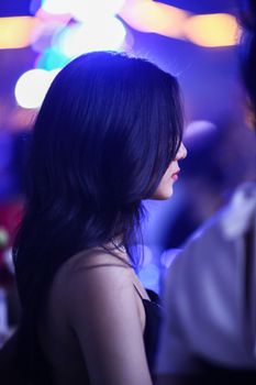 Side profile of a stylish woman at a vibrant, elegant party with dazzling lights.