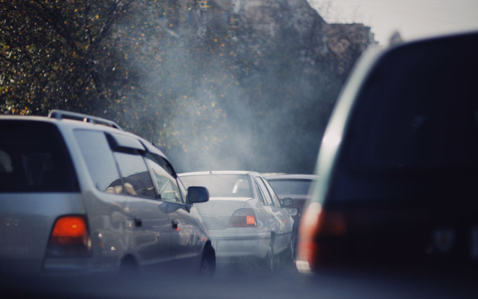 Cars in heavy city traffic with exhaust visible on a busy road