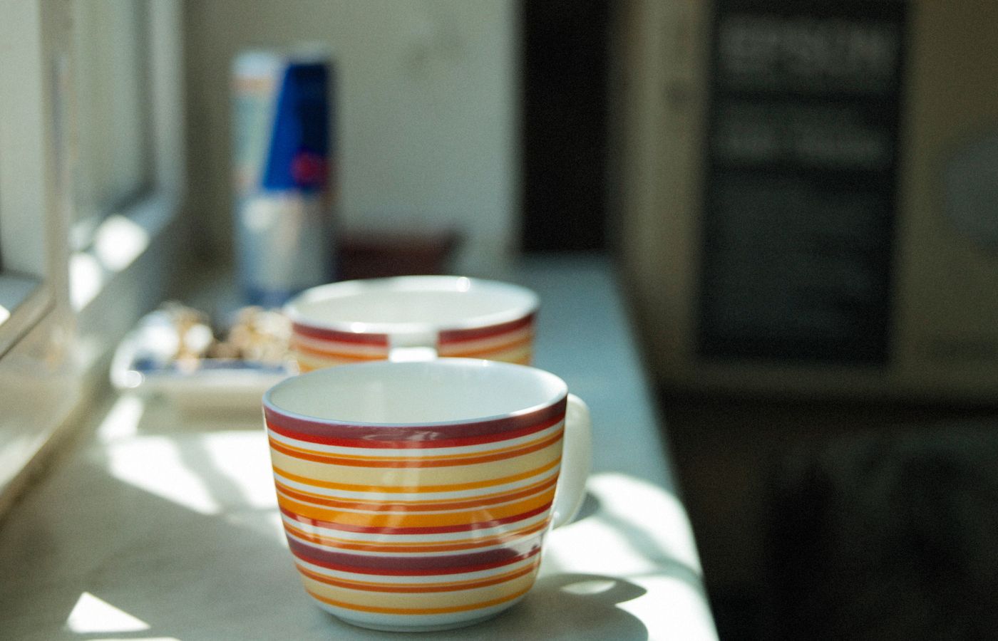 Vibrant ceramic cups with striped patterns on a sunlit kitchen counter.