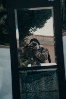 Photographer in camouflage jacket reflected in city mirror.