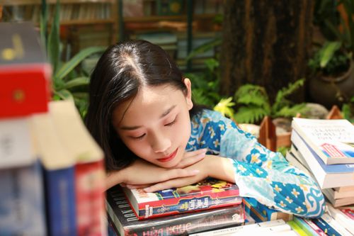 Free A young woman in a blue floral dress resting peacefully on a stack of books indoors. Stock Photo