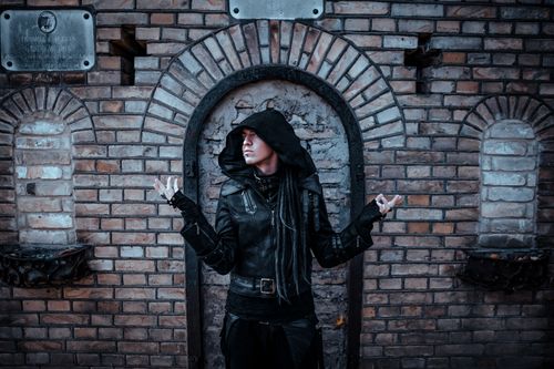 Free Portrait of a mysterious figure in a black hooded leather outfit against a brick wall. Stock Photo