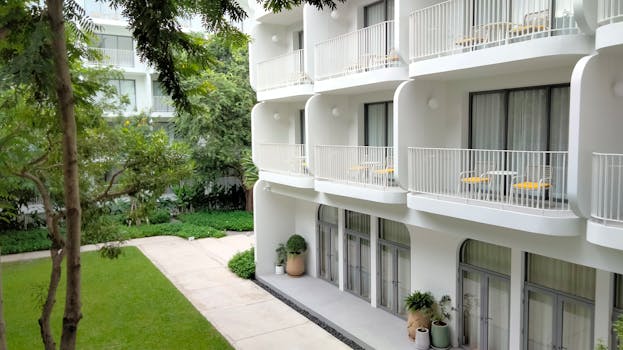 Contemporary white residential building with balconies and lush garden view.