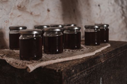 Close-up of glass jars filled with dark homemade preserves displayed on a vintage wooden surface.