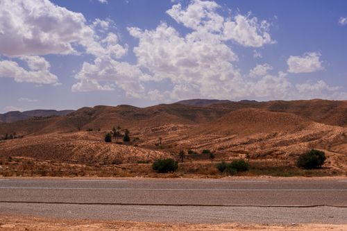 Free A scenic view of desert hills under a vibrant blue sky with fluffy white clouds. Stock Photo