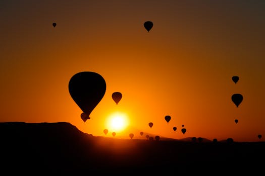 Silhouetted hot air balloons float over Cappadocia during a vibrant sunrise.