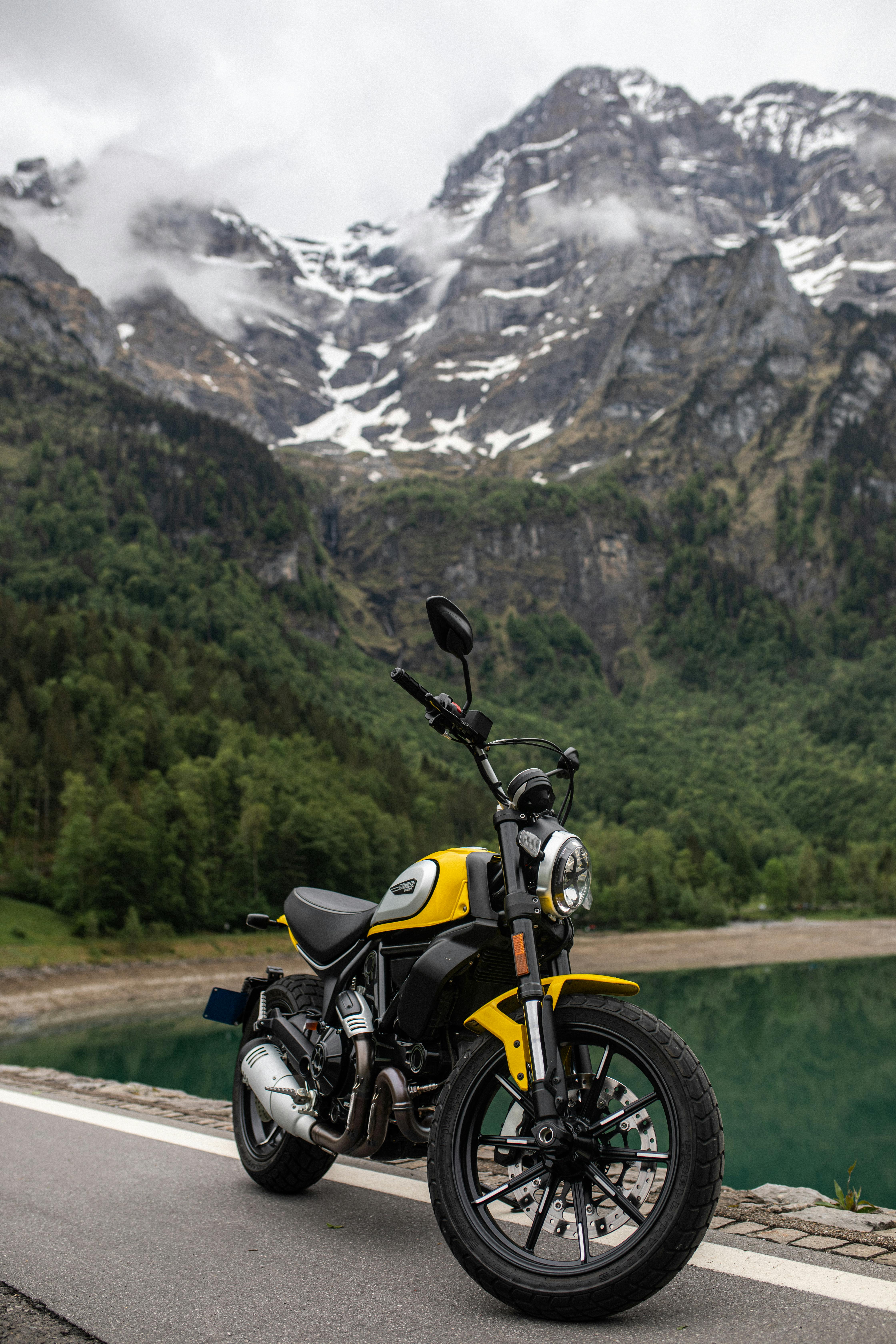 A yellow motorbike parked near a serene mountain lake with stunning alpine scenery.