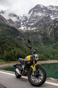 A yellow motorbike parked near a serene mountain lake with stunning alpine scenery.