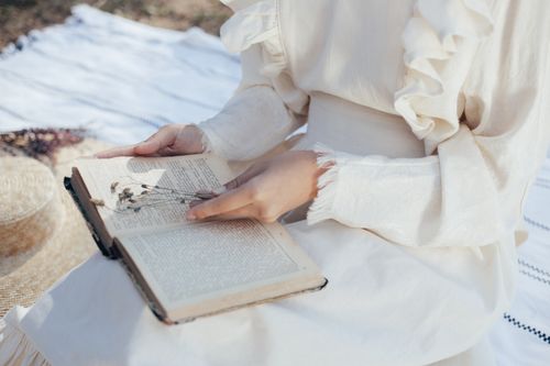 Free Woman in a white dress reading a vintage book in a serene outdoor setting, evoking a sense of nostalgia and tranquility. Stock Photo