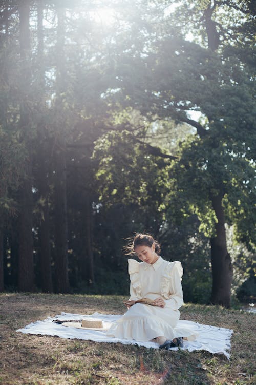 Young Woman in White Dress Reading Book in Park