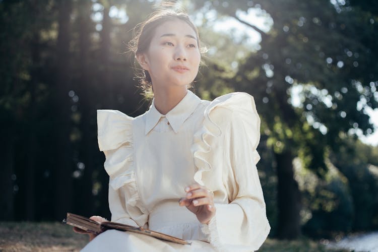 Young Woman In White Dress Holding Book In Park