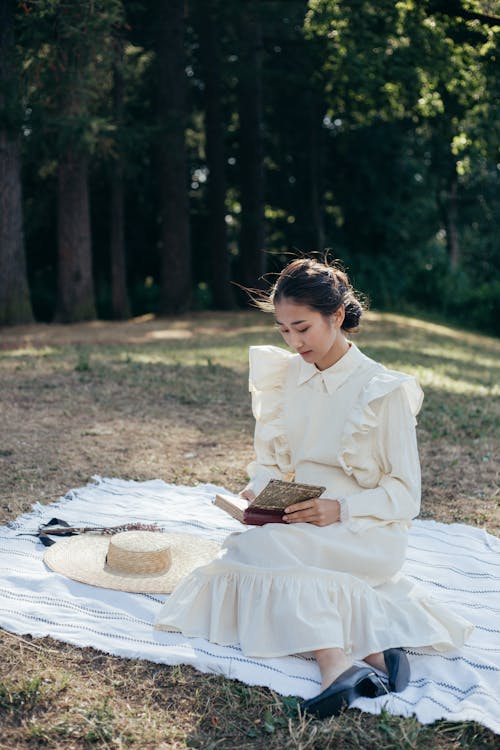Young Woman in White Dress Reading Book in Park