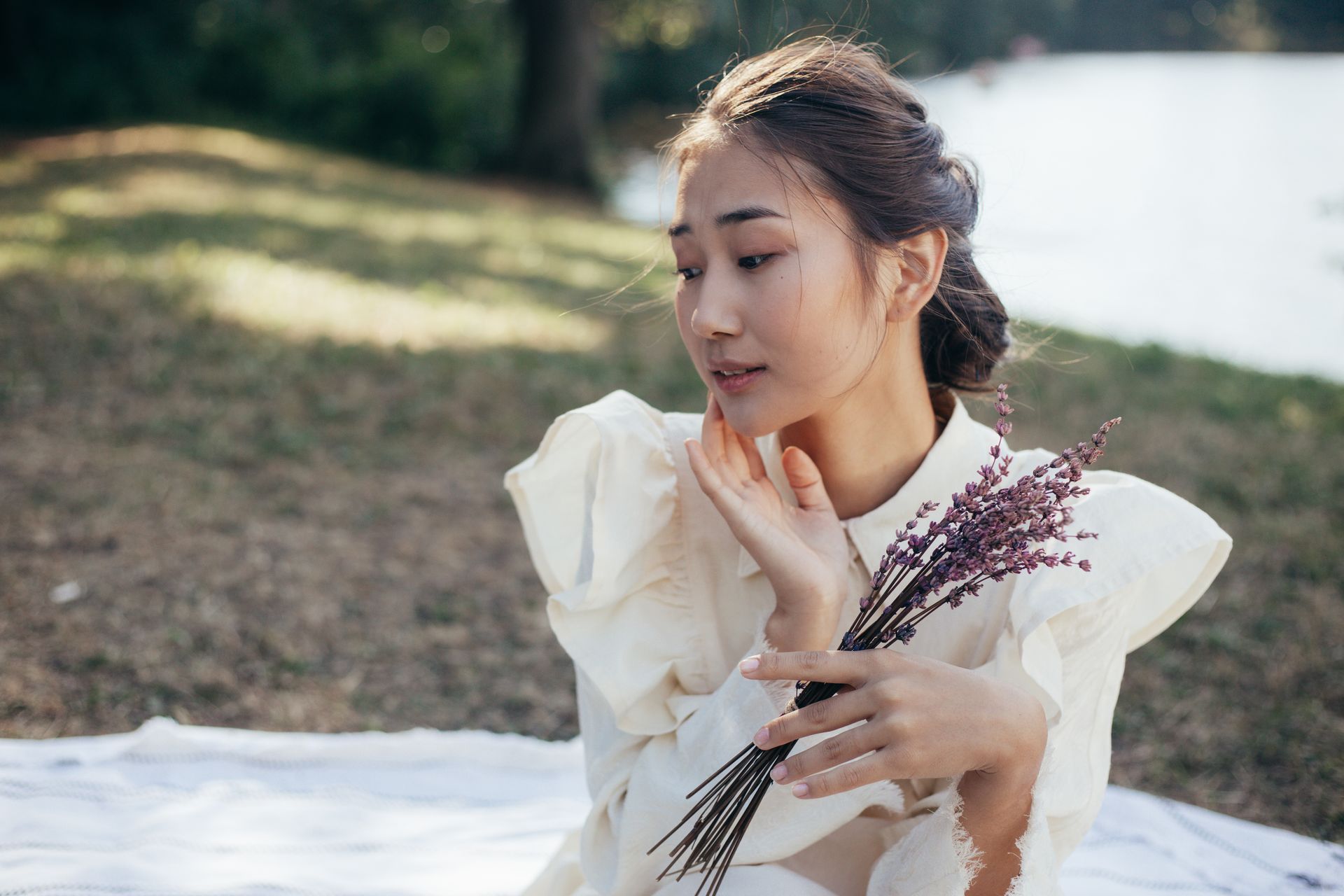 A young woman enjoys a tranquil moment holding lavender outdoors.