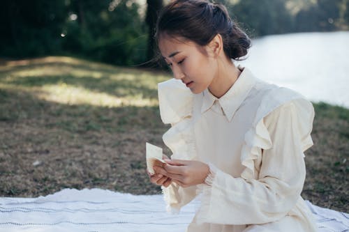 Free Young Woman in White Dress Holding Letter in Park Stock Photo