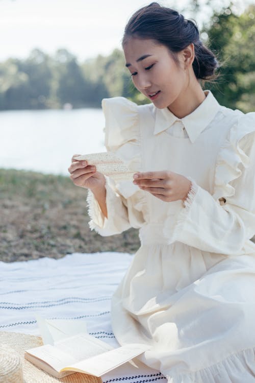 Free Young Woman in White Dress Reading Letter in Park Stock Photo