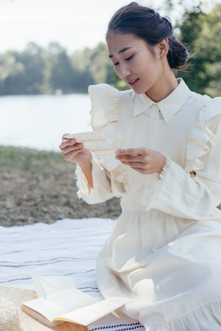 Young Woman In White Dress Reading Letter In Park