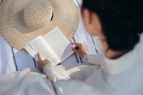 Free A woman leisurely reads a book on a picnic blanket with a straw hat, conveying tranquility and nostalgia. Stock Photo