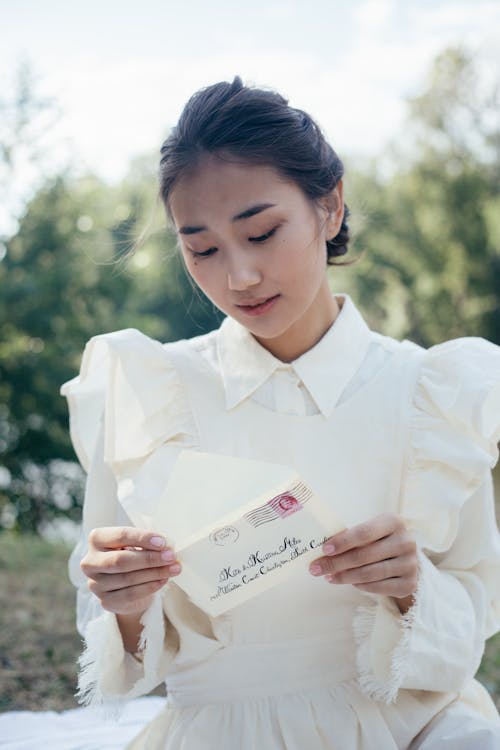 Young Woman in White Dress Reading Letter in Park