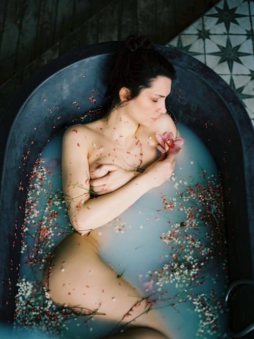 Naked Woman Lying on Back in Bathtub with Flowers