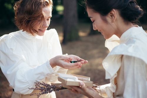 Free A heartwarming outdoor exchange of a butterfly gift between two women in vintage attire. Stock Photo