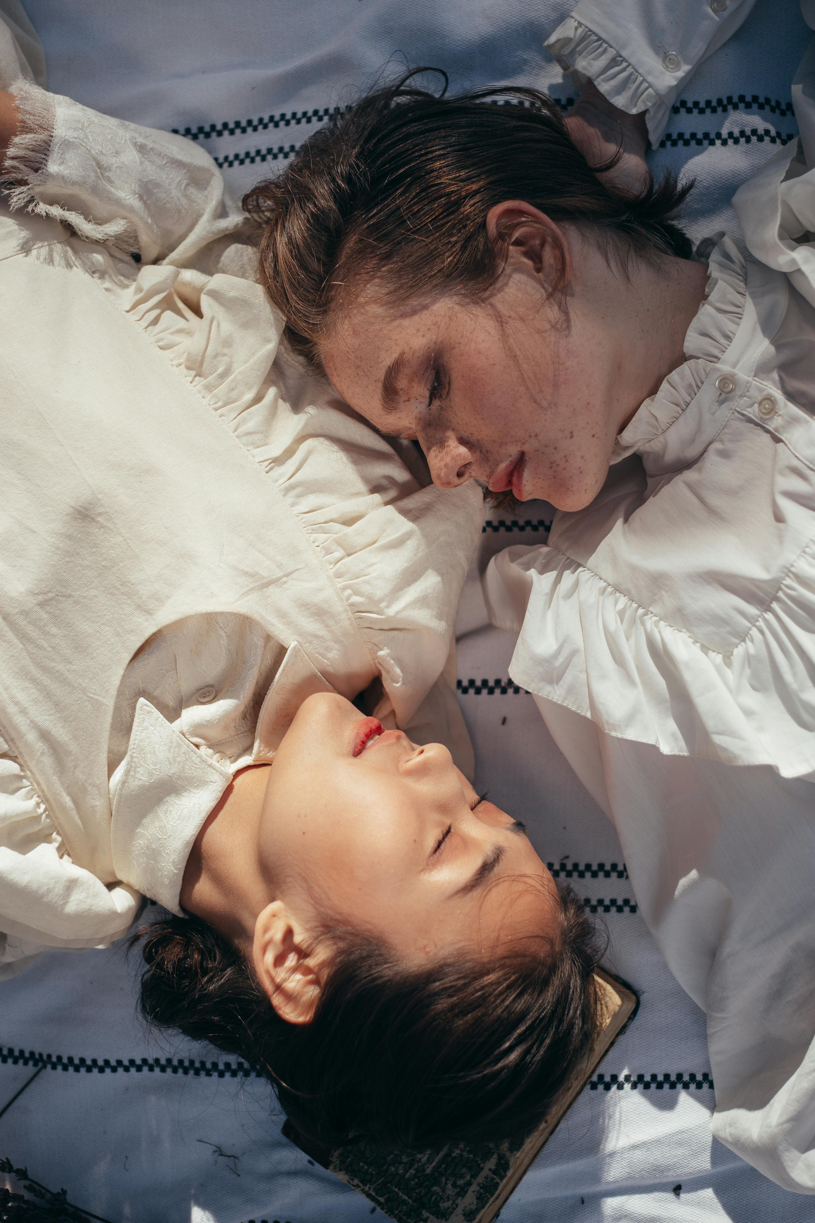 women in old fashioned clothing lying face to face on picnic blanket