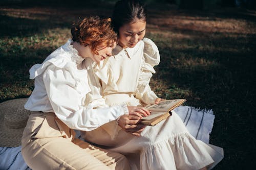 Free Women in Old-Fashioned Clothing Reading Book on Picnic Blanket Stock Photo