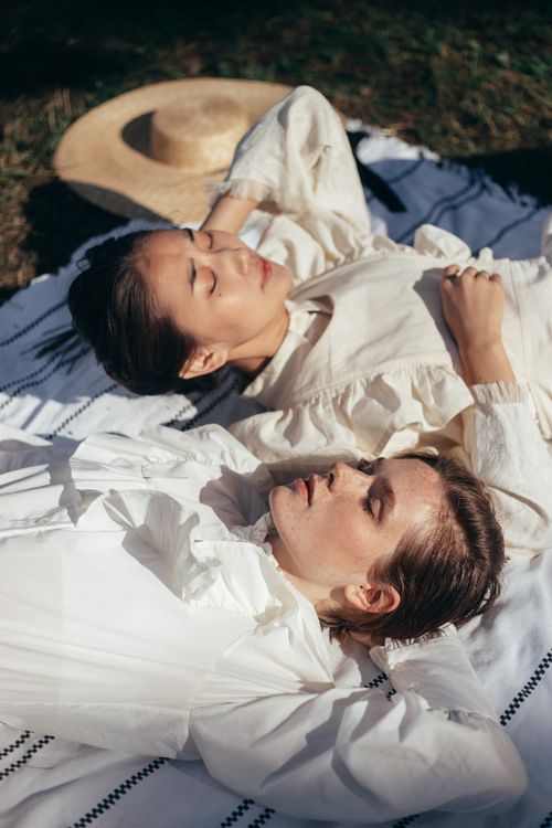 Free Two women lying on a picnic blanket, eyes closed, enjoying a sunny day outdoors. Stock Photo