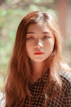 A beautiful portrait of a young woman with long hair and natural makeup in a serene outdoor setting.