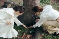 Woman in White Dress Shirt and Black Pants Sitting on Tree Trunk
