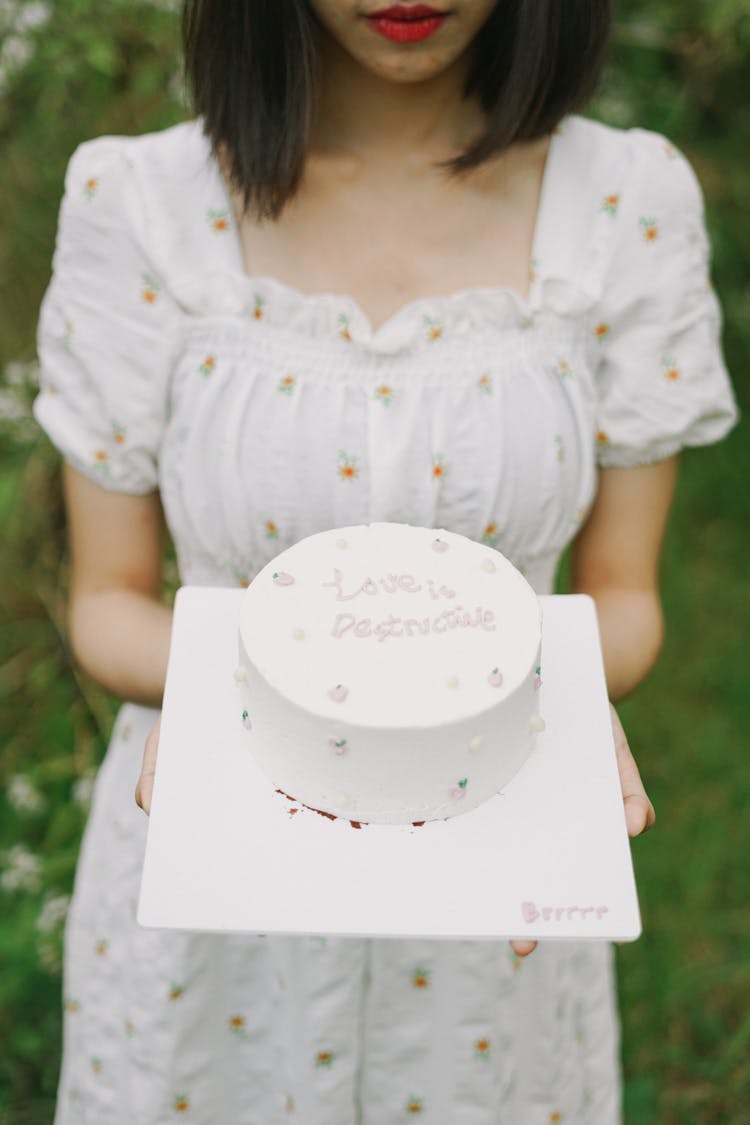 Woman In Long Dress Holding Cake Decorated With Writing On White Tray