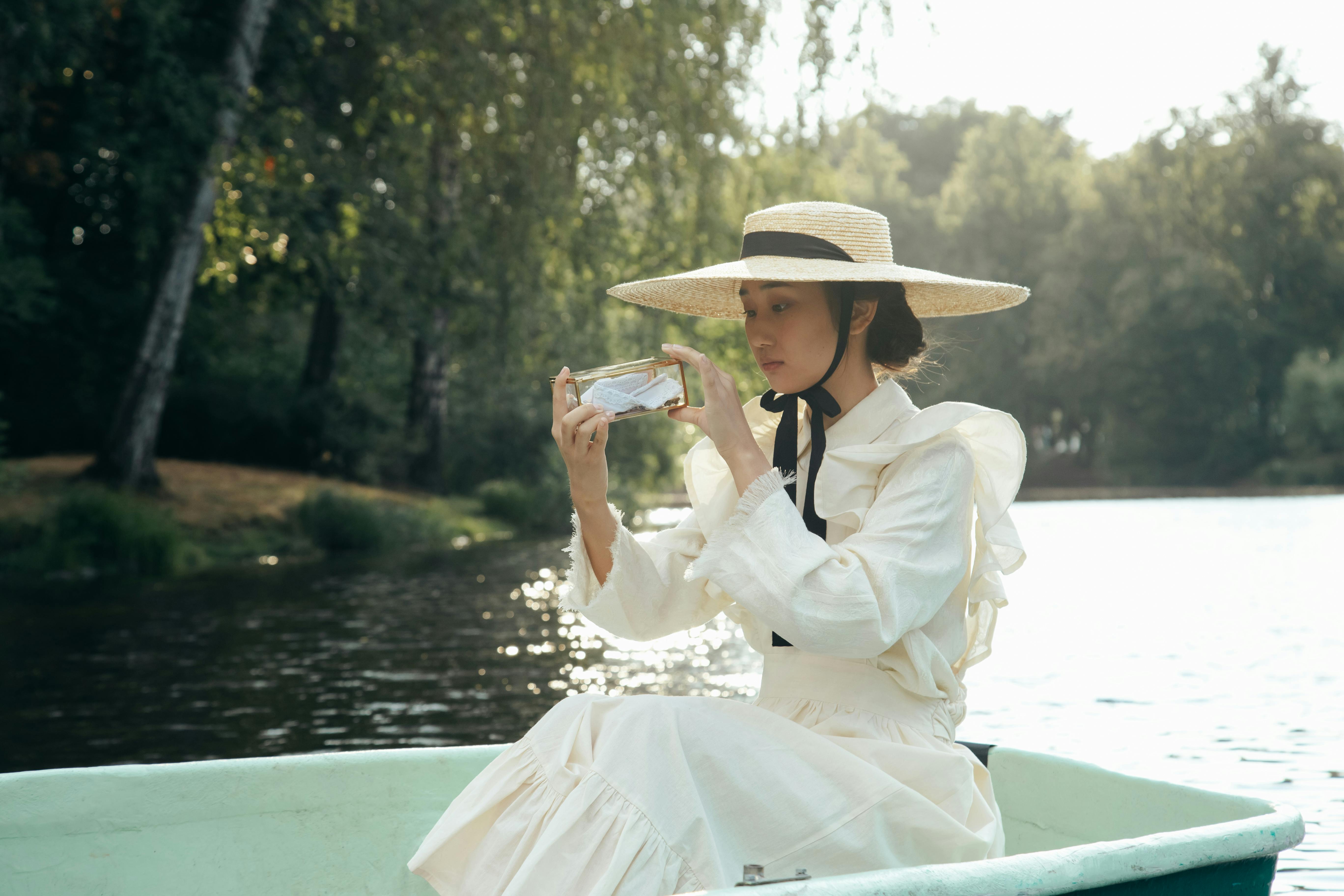 Elegant woman in a vintage dress and hat relaxing on a boat by the lake.