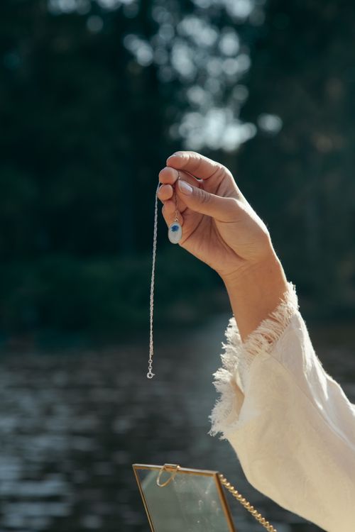 Free Close-up of a hand holding a pendant against a serene lake backdrop, showcasing tranquility and elegance. Stock Photo
