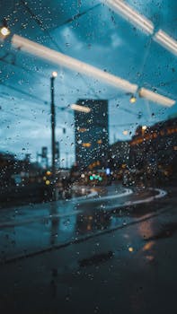 Raindrops on a window create artistic patterns while revealing a blurred night cityscape.
