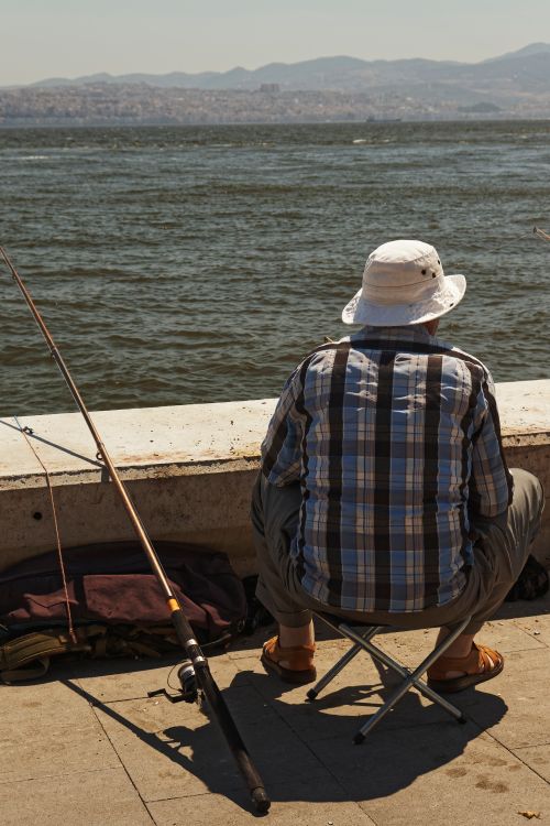 Free A man enjoys fishing by the seaside, a peaceful hobby under a clear sky. Stock Photo
