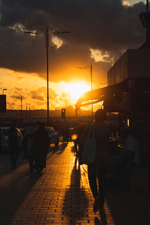 Free Silhouettes walking along a sunlit sidewalk during a beautiful sunset with dramatic clouds. Stock Photo