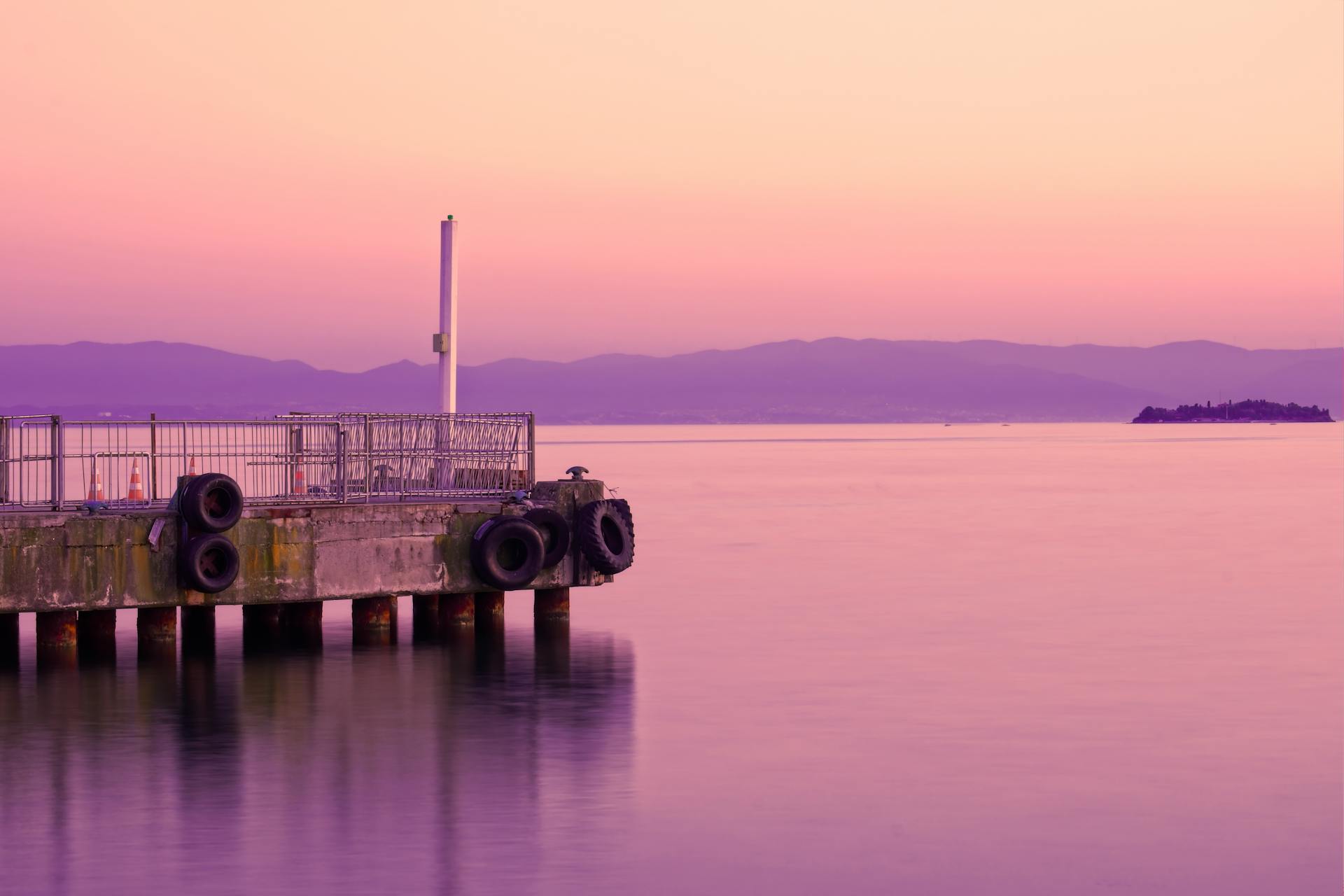 A tranquil pink sunset over a calm sea with a concrete dock in view.