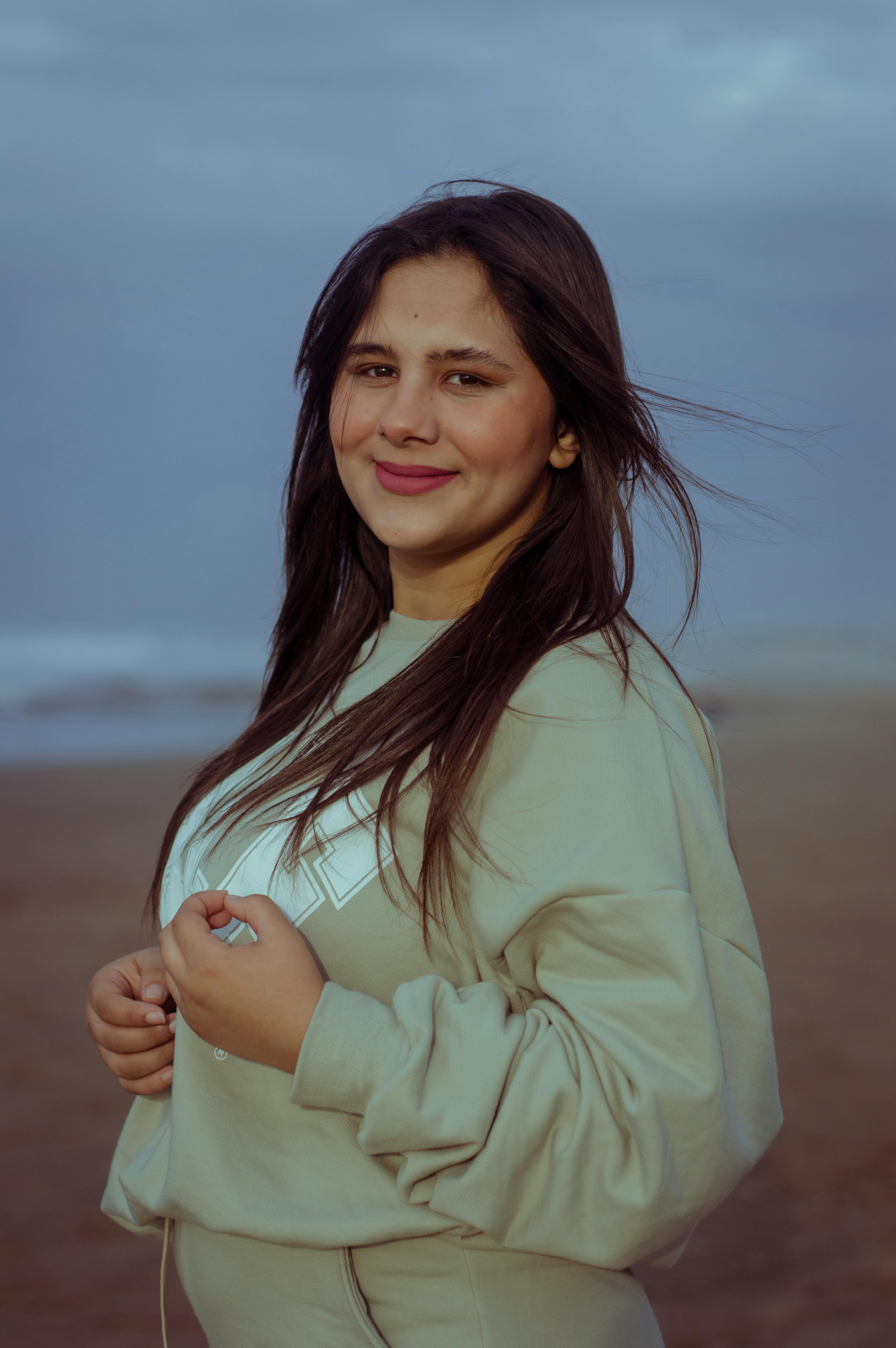Portrait of a smiling woman in a sweater on a Casablanca beach at sunset.