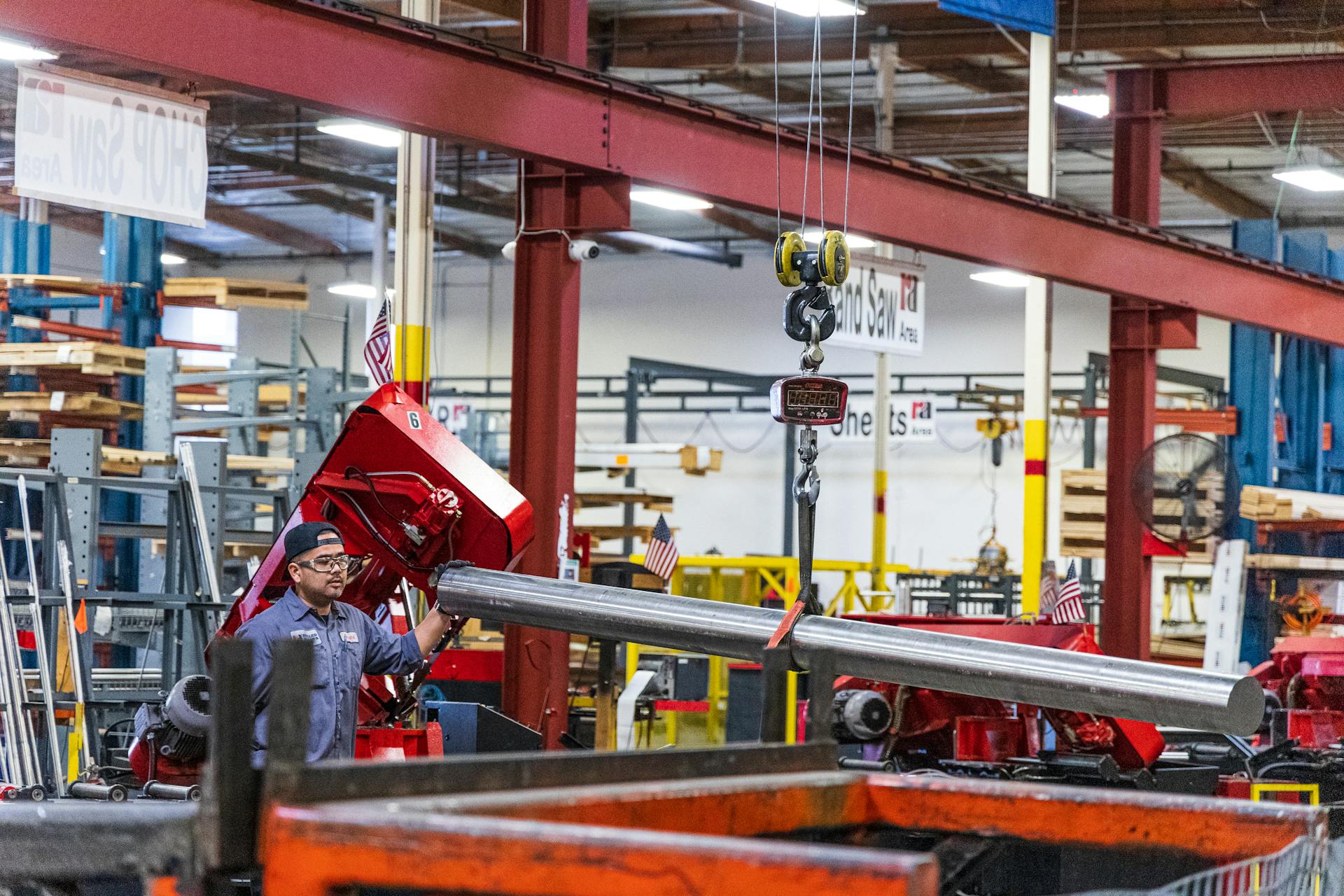 Worker operating heavy machinery in a factory, moving steel bars. Industrial scene indoors.