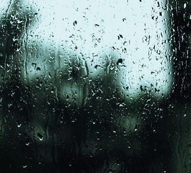 Close-up view of rain droplets on a glass window creating a blurry, moody background effect.