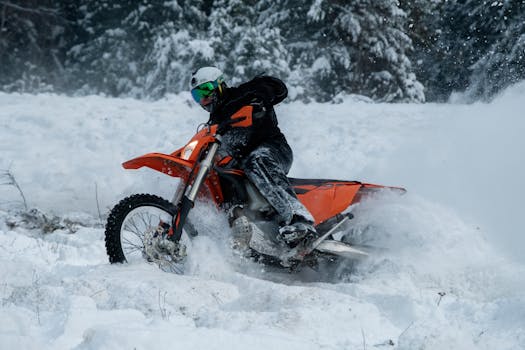 Motorcyclist in dynamic winter action riding through snow-covered forest landscape.
