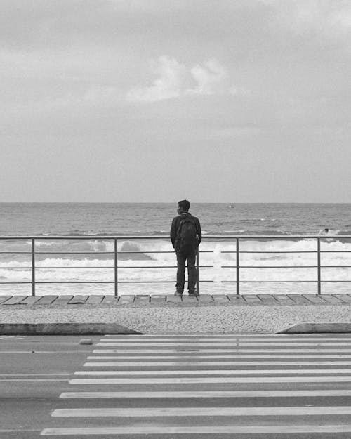 Free Man Standing on a Sidewalk Beside the Sea Stock Photo