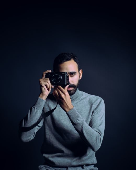 Portrait of a bearded photographer holding a camera in a studio setting, capturing the moment.