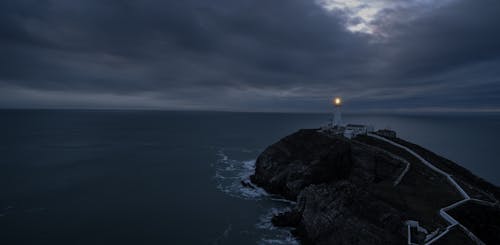 White Lighthouse on Black Rock Formation Near Body of Water