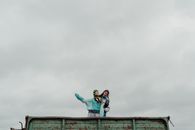 Man in Green Jacket and Blue Denim Jeans Jumping on Brown Wooden Fence Under White Cloudy