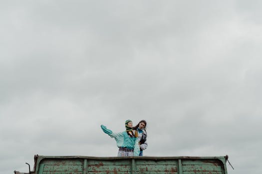 Two adults standing on an industrial vehicle under a cloudy sky.