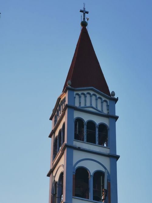 Free A church tower with a red roof stands tall against a clear blue sky. Stock Photo