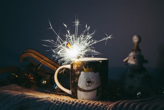 A cozy winter scene featuring a festive mug with a bear design, alit with a bright sparkler, surrounded by Christmas decorations.