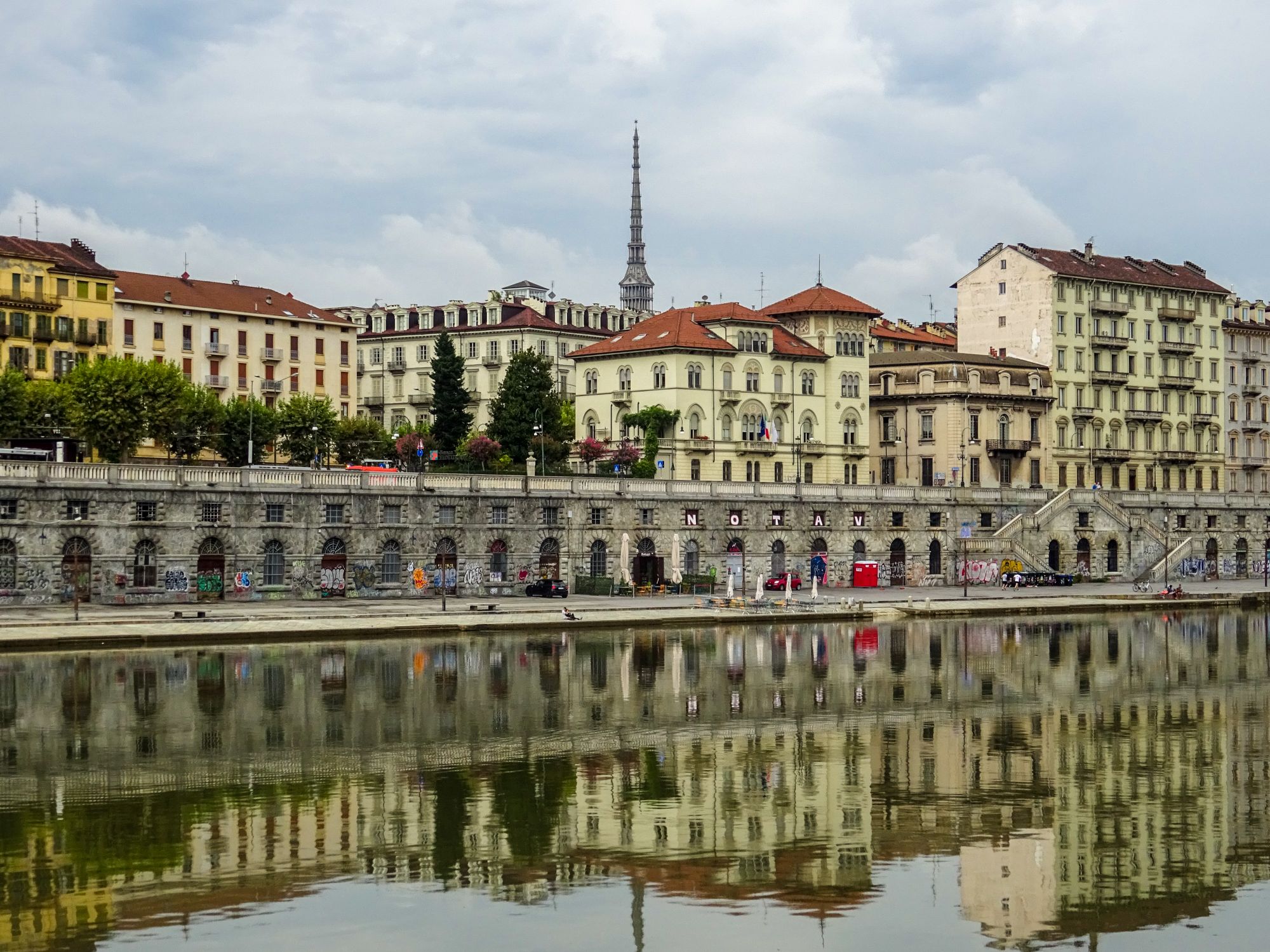 Scenic view of Turin's historic architecture reflected in the river under an overcast sky.