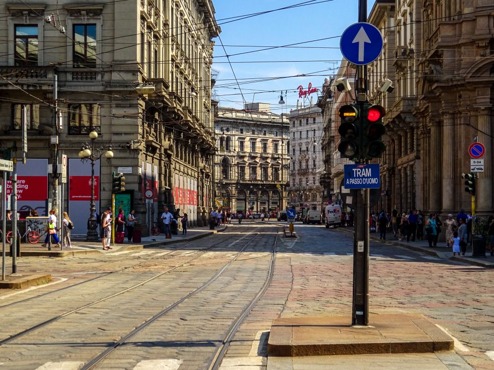 Stradă aglomerată din Milano, cu arhitectură istorică și linii de tramvai