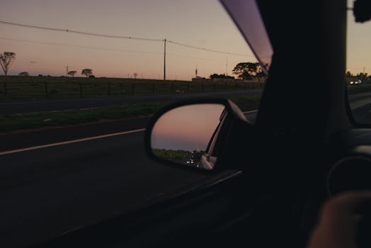 Captivating sunset view in side-view mirror during highway drive, with open road and serene sky.